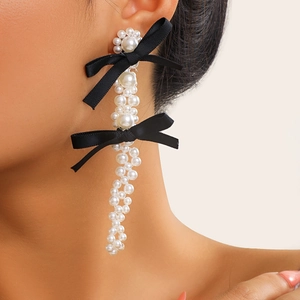 Close-up of elegant long pearl fringe earrings with black ribbon bows on a female model