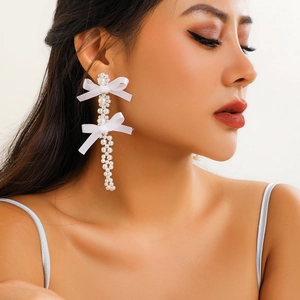 Detail view of long pearl drop earrings with elegant white satin ribbon bows on model