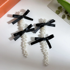 Detail of drop earrings with white pearls and black satin bows in a retro style