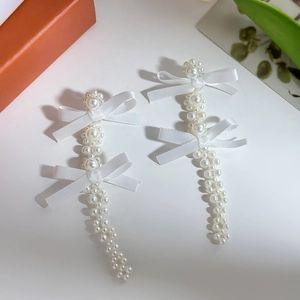 Detail of white satin bow earrings with cascading imitation pearl tassels and floral accents