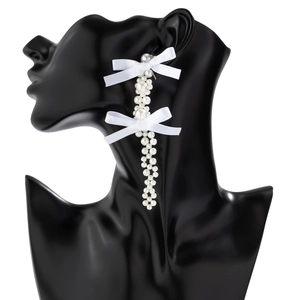 Close-up of white fabric bow earrings with long hanging faux pearls on a black display
