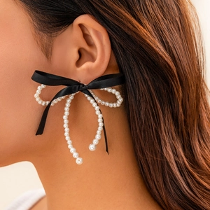 Detail of elegant black ribbon bow earrings with white pearl ring drops on model