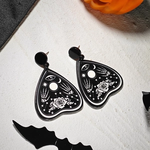 Close-up of black and white gothic planchette earrings with spooky occult patterns