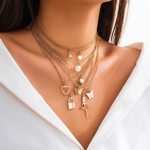 Dettaglio di una collana dorata a strati con ciondoli a farfalla, cuore e perle