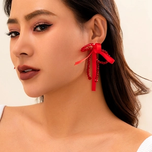 Macro view of red beaded bow earrings with satin ribbon tassels on a female model