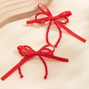 Detail of red ribbon bow earrings with faceted beads and festive fabric texture