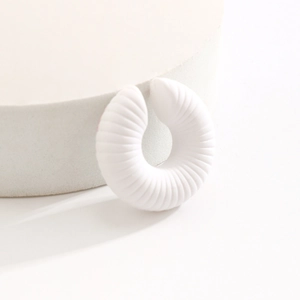 Dettaglio di un ear cuff bianco opaco a forma di C con fine trama a coste e design minimalista