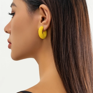 Dettaglio del lobo con ear cuff a forma di C gialla e superficie a coste testurizzata