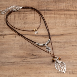 Detail einer mehrlagigen Boho-Halskette mit silbernen Blattanhängern auf Webseilen