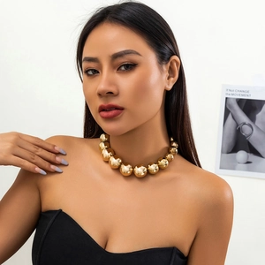 Gros plan d'un collier à grosses perles dorées porté par un mannequin en robe noire