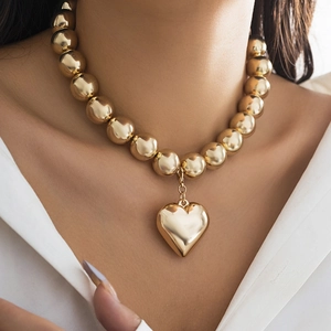 Detail of chunky gold bead necklace with bold 3D heart pendant on model neckline
