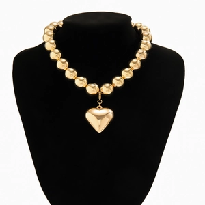 Close-up of polished gold bead collar necklace with a solid heart pendant on display