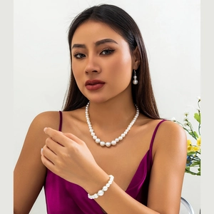 Driedelige set van elegante barokke parelketting, armband en oorbellen op paarse jurk