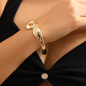 Dettaglio di un bracciale dorato irregolare con design astratto in metallo liquido al polso