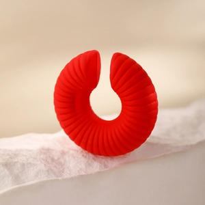 Dettaglio macro di un earcuff rosso a forma di C con texture radiale su base in pietra