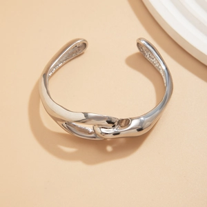 Dettaglio bracciale rigido in argento lucido con fibbia geometrica in metallo intrecciato