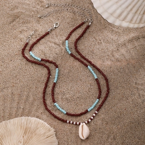 Detail of beach necklace with red and blue beads and a natural white conch shell pendant