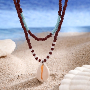 Detail of bohemian double-layer beaded necklace with natural cowrie shell on beach sand