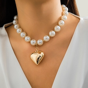 Close-up of a large pearl necklace featuring a polished golden heart-shaped pendant on neck