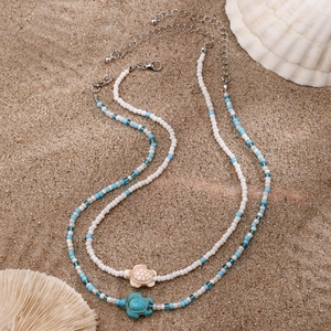 Handmade seed bead necklace set with turtle pendants on a summer beach sand background