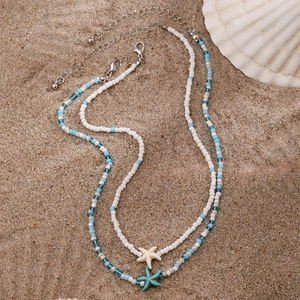 Detailed view of two handmade bead necklaces with starfish pendants on sandy background