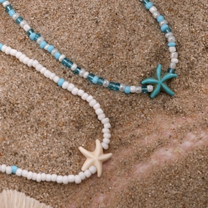Detail of beach style beaded necklaces with starfish pendants on white sand background