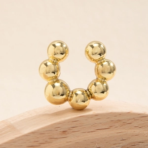 Dettaglio macro di un earcuff a forma di C placcato oro con sette sfere lucide su legno