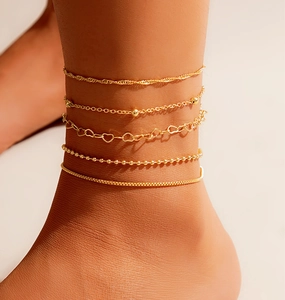 Detail of five layered gold anklets featuring heart charms and beads on an ankle