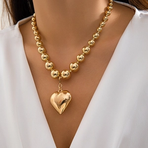 Close-up of golden beaded choker necklace featuring a large polished heart pendant on model