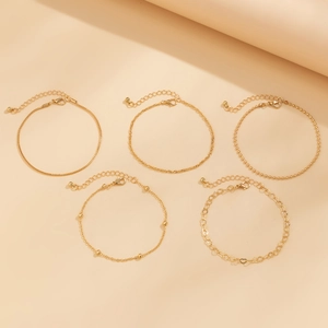 Detail view of five gold-plated layered anklets with diverse chain styles and lobster clasps
