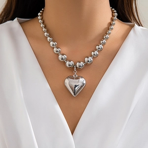 Detail view of a thick silver ball chain necklace with a large 3D heart pendant on a model