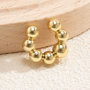 Dettaglio di un earcuff dorato a sfere con sette sfere metalliche lucide su base legno