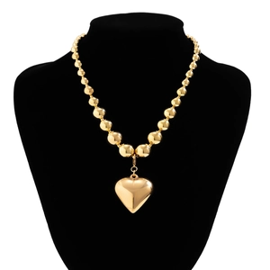 Detail of gold beaded necklace featuring a large polished 3D heart pendant on black stand