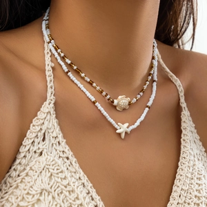 Detail of layered beach necklace featuring white beads with sea turtle and starfish pendants