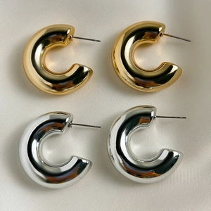 Makroaufnahme von klobigen C-förmigen Creolen in poliertem Gold- und Silber-Metall-Finish