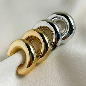 Nahaufnahme polierter C-förmiger Chunky-Ohrringe in Gold und Silber auf weißer Seide