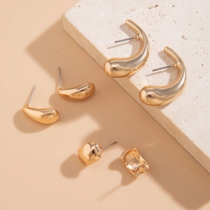 Nahaufnahme von goldenen geometrischen Ohrringen mit polierten Tropfen- und Creolen-Sets