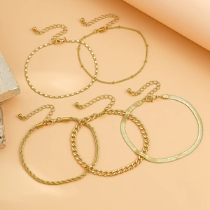 Detail of five-piece gold punk anklet set including curb and snake chains on stone