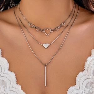 Detail of layered silver necklaces with heart charms and a vertical bar on a model