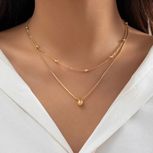 Détail d'un collier doré à deux rangs avec perles et pendentif goutte porté par un mannequin