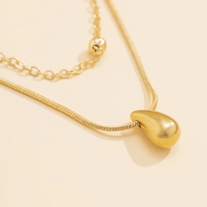 Détail macro d'un collier double couche doré avec pendentif goutte miroir et perles fines