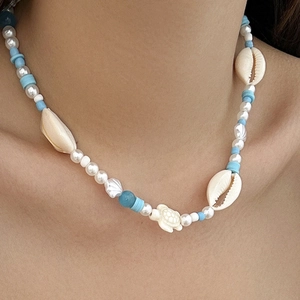 Detail of beach necklace with blue beads, sea turtle and seashell charms on model