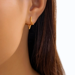 Close-up of a minimalist gold star hoop earring worn on a model against a white background