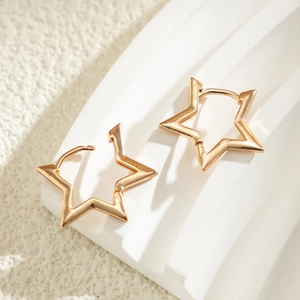 Macro shot of minimalist gold star hoop earrings on a textured white display stand