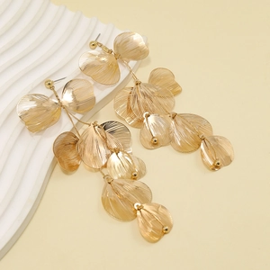 Détail de longues boucles d'oreilles feuilles dorées avec texture en métal brossé