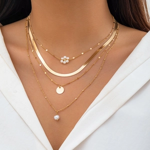 Detail of layered gold necklaces with pearl charms and sleek snake chain on white shirt