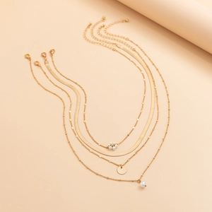 Detail of multi-layered gold snake chain and beaded necklace with pearl flower charms