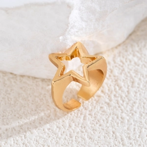 Macro shot of gold hollow star open ring on white stone, minimalist polished metal jewelry