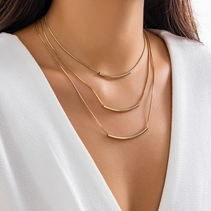 Close-up of three-layered gold snake chains with minimalist curved arc bar pendants