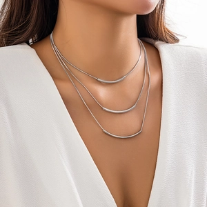 Close-up of triple-layered silver snake chains with minimalist curved metal tube pendants